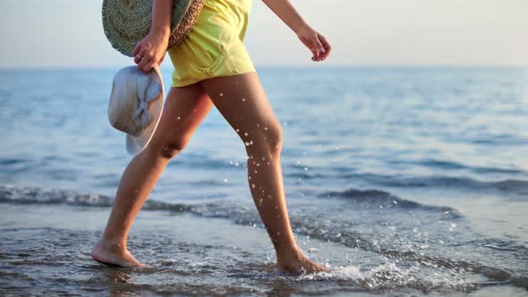 Closeup Female Legs Going on Sand Beach Near Sea with Straw Hat and Handbag