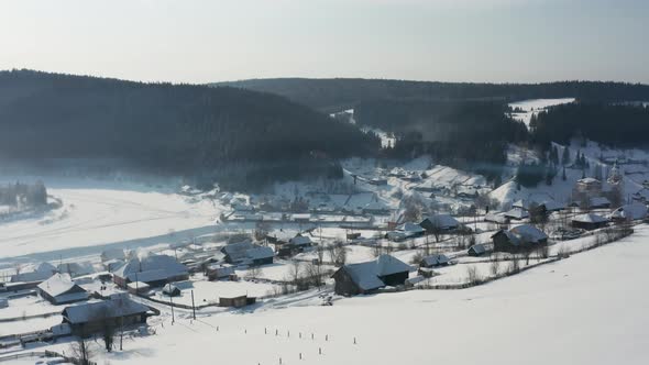 Aerial View of a Village with Wooden Houses on the Bank of a Frozen River in Winter