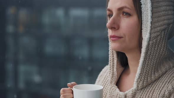 Caucasian Woman Stays on Balcony During Snowfall with Cup of Hot Coffee or Tea