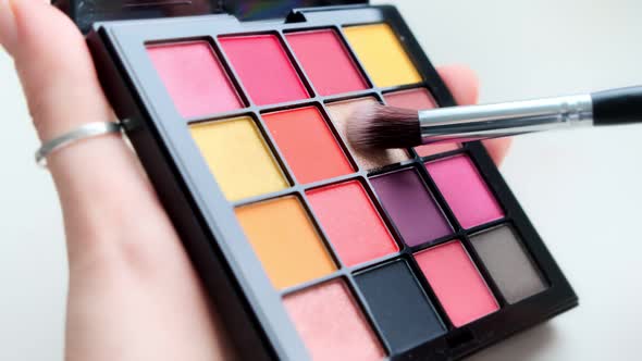 Close up a palette with colorful eye shadows and a makeup brush