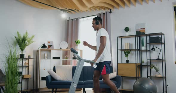 African American Guy Enjoying Music in Headphones while Training on Running Track at home