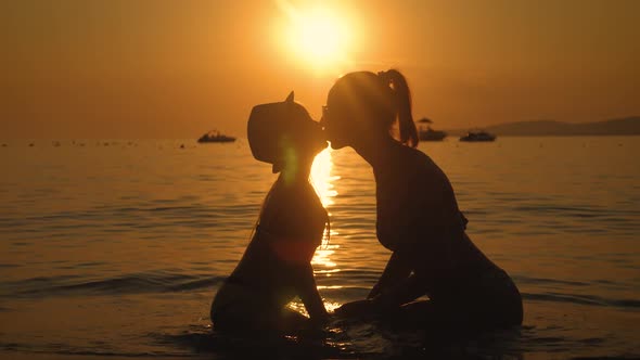 Silhouettes Mother and Daughter Sit on the Beach at Sunset. Concept of Friendly Family, Lifestyle
