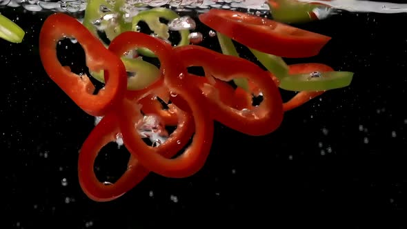 Tasty Peppers Slices Fall Down Into Clear Water on Black