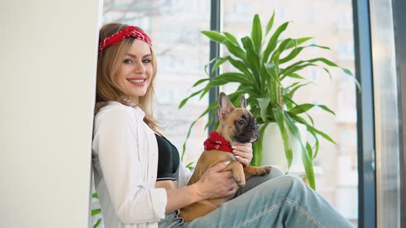 Beautiful Woman with a French Bulldog Dog in Her Arms Sitting and Looking Directly in Camera