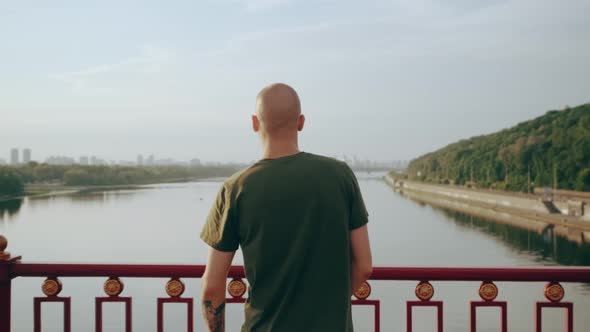 Young Man Stretches While Standing on Footbridge Overlooking the River