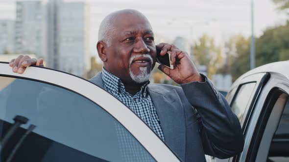 Mature African American Businessman Standing Near Car Outdoors in Parking Lot Speaks on Mobile Phone