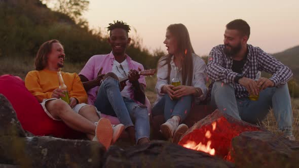 Friends is Sitting Around Campfire Drinking Craft Beer and Smiling