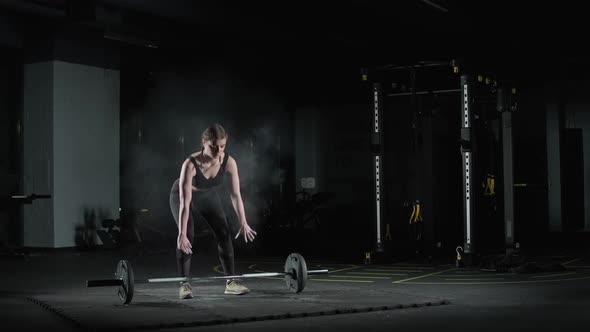 Female Fighter Performs a Deadlift with Barbell Lifts Barbell and Does Weights Training in the Gym