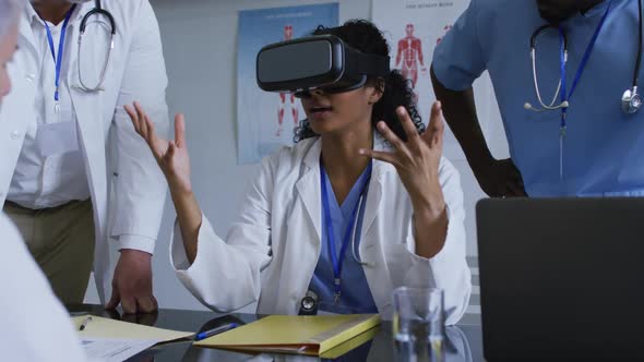 Asian female doctor at table using vr headset with a diverse group of colleagues gathered around her