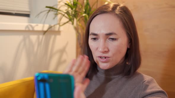 a Woman Looks at the Smartphone Screen and Waves Her Hand