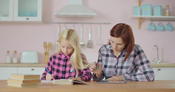 Working Mother Using Tablet Computer and School Girl Making School Homework Nearby. Family Working