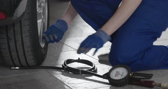 Female mechanic doing a car service in the auto repair shop, she is checking tire pressure