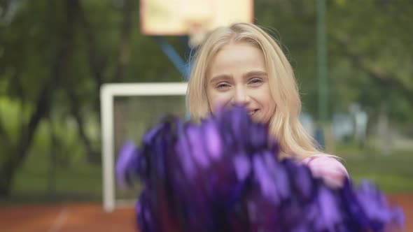 Close-up of Cheerful Blond Woman Shaking Pom-poms and Laughing. Portrait of Joyful Young Cheerleader