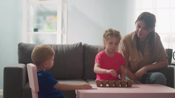 Young Woman Watches How Children Plant Seeds of Home Plants