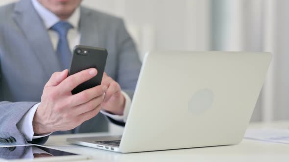 Close Up of Businessman with Laptop Using Smartphone