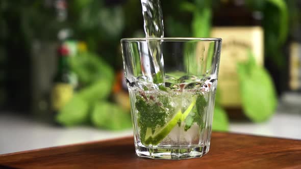 Slow Motion Mineral Water or Soda Fill Glass with Lime, Mint and Ice Cubes. Food Background.