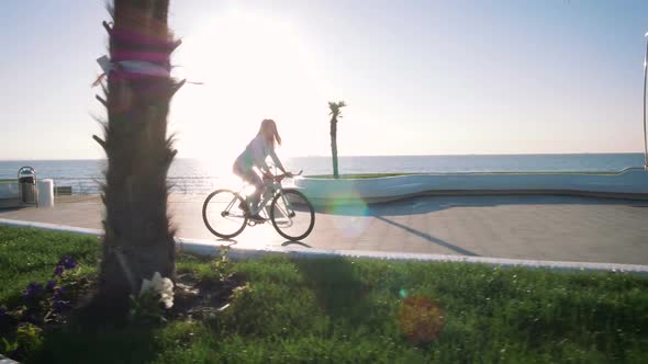 Young Stylish Woman Cyclist Enjoying Fixed Gear Bike Riding Outdoors at Sunrise Near the Sea