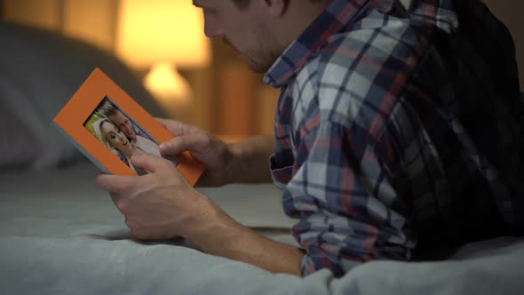 Young Man in Despair Lying on Bed Looking at Photo With Girlfriend, Sadness