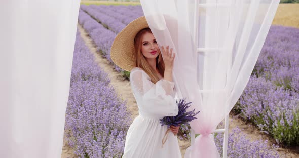 Beautiful Girl in a Hat with a Bouquet of Lavender Near the Gazebo