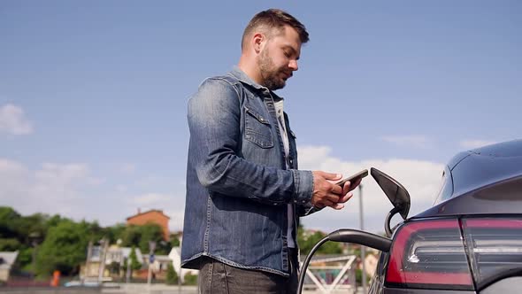 Man Controlling the Time on Phone while Charging Battery on His Lux Class Electric Car