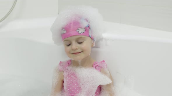 Cute Blonde Girl Takes a Bath in Swimwear. Little Child Washes Her Head