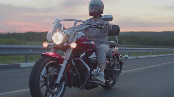 Woman rides cool motorcycle with glasses and helmet. Woman on red motorbike rides on highway.