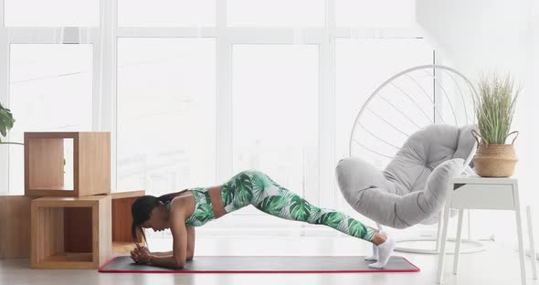 Slim black woman standing in plank position at home.