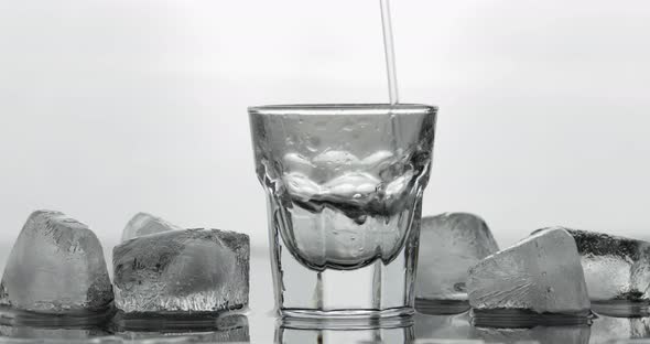Pouring Up Shot of Vodka From a Bottle Into Glass. White Background