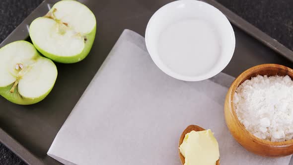 Bowl of sugar and apple, flour with butter in spoon