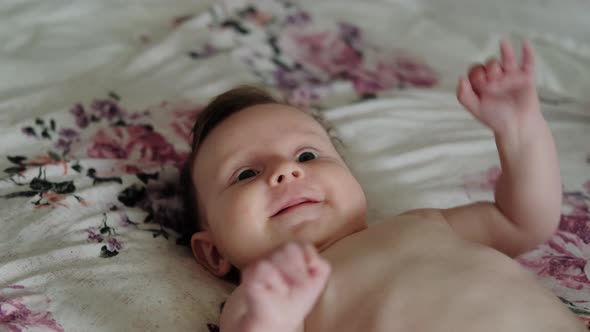 The Baby is Lying on the Bed and Smiling at the Camera