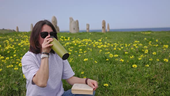 The Girl Drinks Tea Sitting on the Green Grass