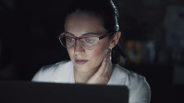 Business Woman Wearing Glasses Working on a Laptop in a Dark Office