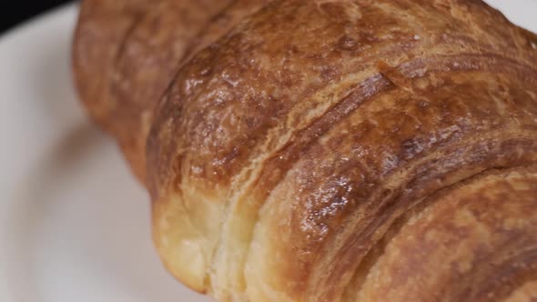 Croissant on white plate rotating in front of camera on black background