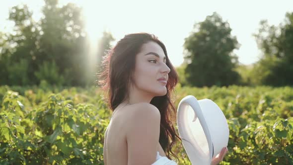 Pretty Girl Smiling Undresses and Putting on Hat on Head Among Plantation