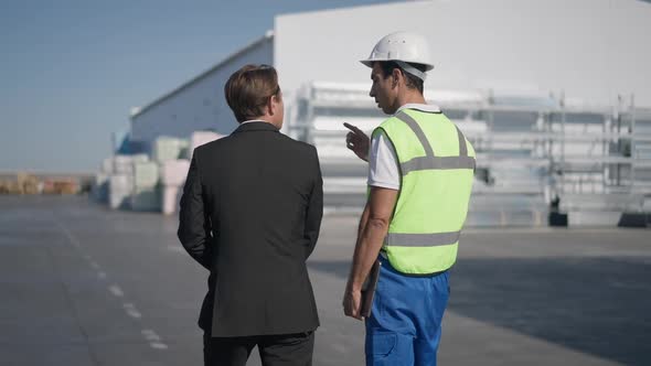 Concentrated Confident Middle Eastern Man in Uniform and Caucasian Warehouse Manager in Suit Walking