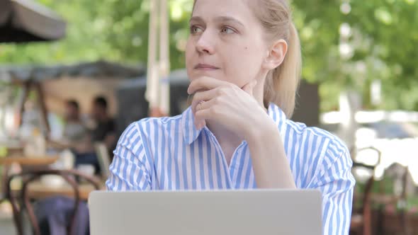 Pensive Young Woman Using Laptop in Outdoor Cafe