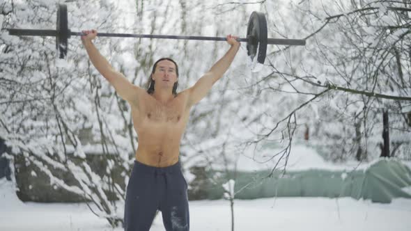 the Guy is an Athlete with Long Black Hair is Engaged in Weightlifting