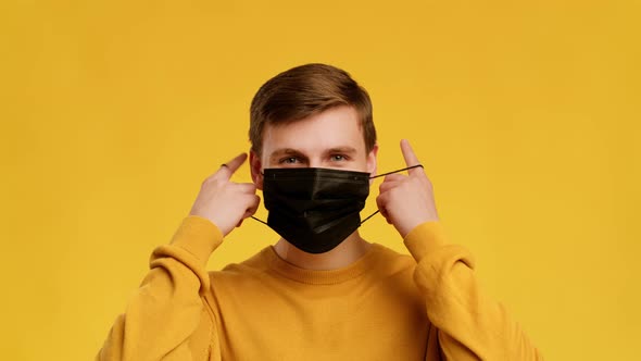 Man Taking Off Face Mask Smiling To Camera Yellow Background