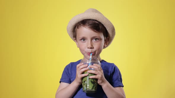 Cute boy Drinking Mojito cocktail From Plastic Cup Over Yellow Studio Background.