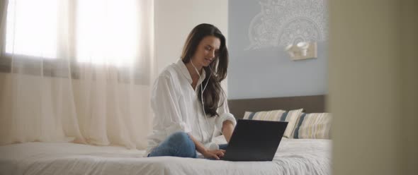 A young woman speaking to someone through earphones while working on her laptop