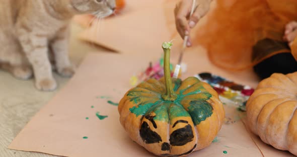 Happy child decorating a pumpkin at home with cat