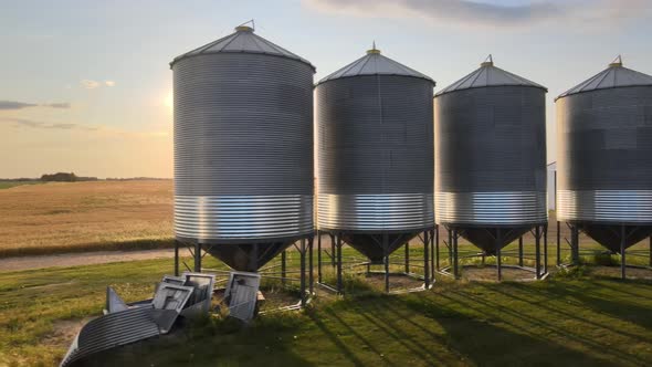 Sidewaysing droneement showing big metal grain bins in rural countryside of Alberta during sunset. 4