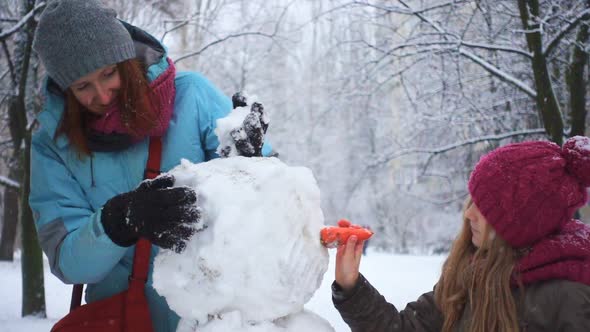 Mother And Her Daughter Playing With Snowman