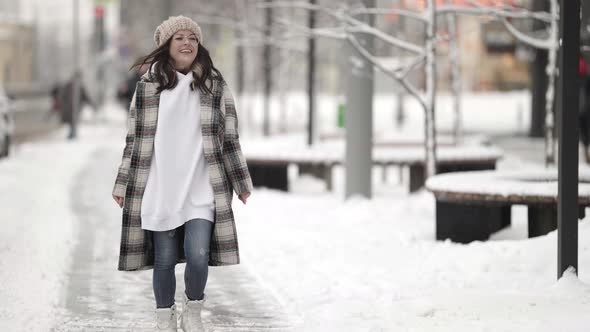 Young Female City Dweller is Walking at Winter Moving Jokingly in Park with Snow Around