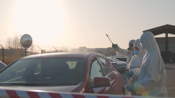 Team of Medical Workers Disinfecting Car and Checking Driver Temperature at Border Entry Point