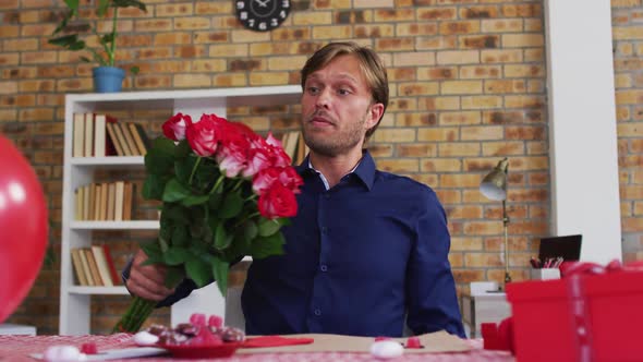Portrait of caucasian man showing a flower bouquet on videocall at home