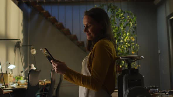 Profile of caucasian female jeweller in workshop wearing apron, using tablet, smiling