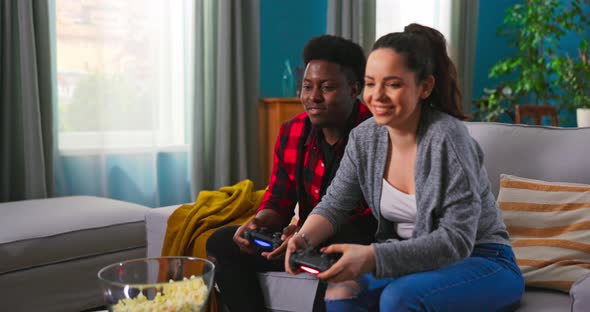 Young Happy Multinational Couple Sitting at Home on Couch and Playing Video Games on Console