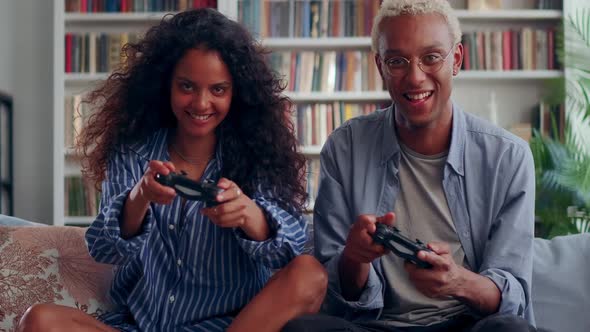 Millennial Couple Holding Controllers Playing Video Games Sit on Couch Indoor