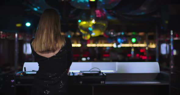Back View of Elegant Young Caucasian Woman in Black Dress Mixing Music in Night Club and Dancing